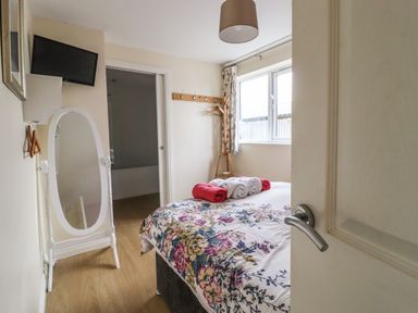 A bedroom with a bed with floral bedding towels on top a mirror and a window at The Old Hen Shed in Hainworth near Haworth
