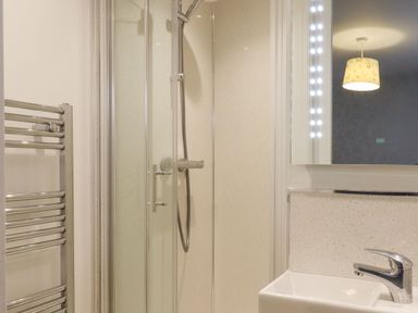 A bathroom with a shower enclosure a towel radiator a sink with a faucet and a lighted mirror at The Old Hen Shed in Hainworth near Haworth