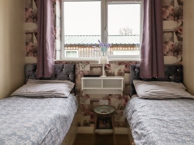 A bedroom with two single beds a window in the middle and a small shelf with a lamp at The Old Hen Shed in Hainworth near Haworth