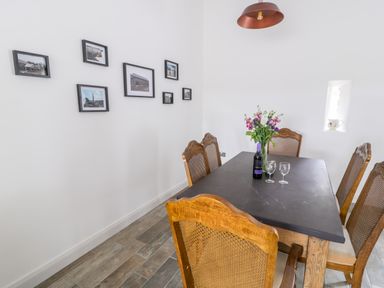 A dining room with a black table and wooden chairs with a flower vase and wine bottle at Storws in Pentraeth