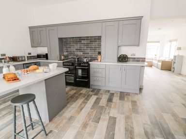 A kitchen with gray cabinets and a black stove with a breakfast counter and stool at Storws in Pentraeth