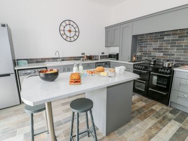 A kitchen with gray cabinets a black stove and a light countertop island with stools and food items at Storws in Pentraeth