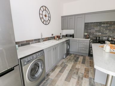 A kitchen with grey cabinets washing machines and a clock on the wall at Storws in Pentraeth