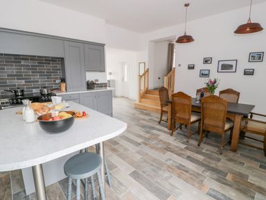 A kitchen with grey cabinets and a white island next to a dining area with a wooden table and chairs at Storws in Pentraeth