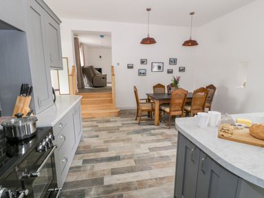 A kitchen with gray cabinets and a dining area with wooden chairs and a table at Storws in Pentraeth