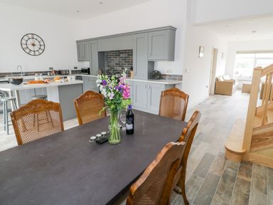 A kitchen and dining area with a black table and wooden chairs with flowers and a bottle on the table at Storws in Pentraeth