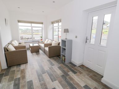 A sitting room with two wicker sofas a glass top table a small bookshelf and a door at Storws in Pentraeth