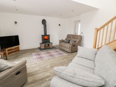A living room with a wood burning stove two sofas a television on a wooden stand and a wooden staircase at Storws in Pentraeth