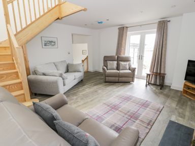 A living room with sofas wooden staircase and glass doors at Storws in Pentraeth