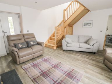 A living room with two sofas a plaid rug wooden staircase and a door at Storws in Pentraeth