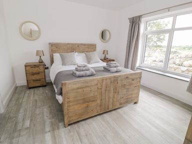 A bedroom with a wooden bed frame two bedside tables with lamps two round mirrors and a large window at Storws in Pentraeth