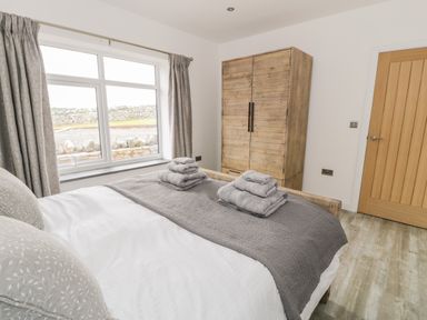 A bedroom with a bed with folded towels on it a wooden wardrobe a window with curtains and a wooden door at Storws in Pentraeth