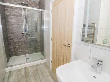 A bathroom with a shower enclosure a wooden door and a sink with a faucet at Storws in Pentraeth