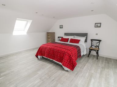 A bedroom with a double bed covered with red plaid bedding two pillows two framed pictures on the walls a wooden chest of drawers a black chair with a lamp and a skylight window at Storws Pentraeth