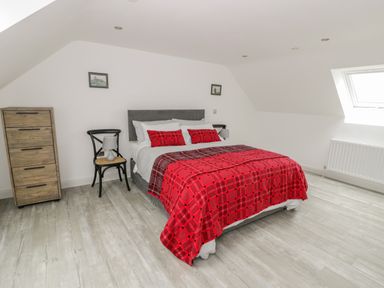 A bedroom with a bed with red bedding two chairs a wooden chest of drawers and a window at Storws in Pentraeth