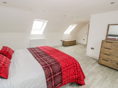 A bedroom with a bed covered in red and black checkered bedding a wooden chest a wooden dresser with a mirror and two skylight windows at Storws in Pentraeth