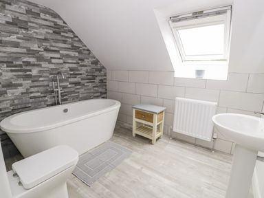 A bathroom with a bathtub toilet sink small table radiator and window at Storws in Pentraeth