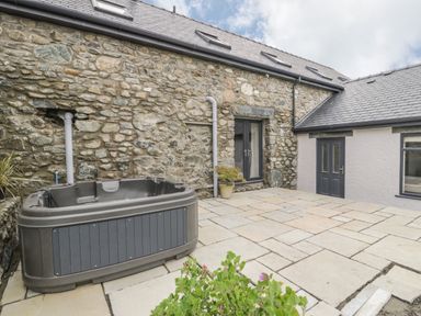An outdoor patio with a hot tub next to a stone wall and a door at Storws in Pentraeth