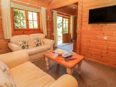 A living room with two sofas a wooden coffee table and a wall-mounted television at Pond Cabin in Stithians