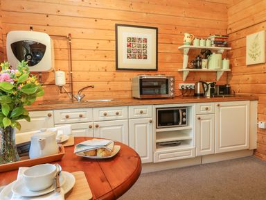 A kitchen with wooden walls white cabinets a microwave toaster oven kettle and a table with a teapot and scones at Pond Cabin in Stithians