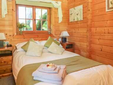 A bedroom with a bed pillows bedside tables and a window at Pond Cabin in Stithians