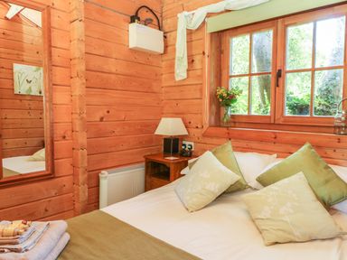A bedroom with a bed covered with pillows and towels beside a wooden wall and window at Pond Cabin in Stithians