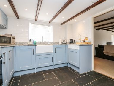 A kitchen with blue cabinets a white sink and microwave at Forge Cottage in Sennen