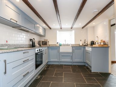 A kitchen with blue cabinets black floor tiles and a white sink at Forge Cottage in Sennen