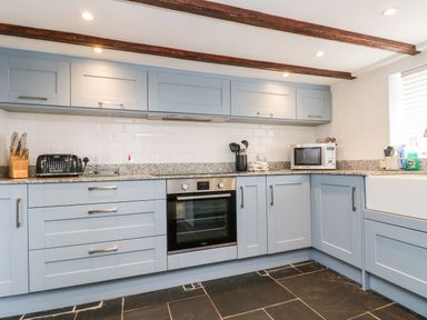 A kitchen with blue cabinets a microwave an oven a toaster and a knife block at Forge Cottage in Sennen