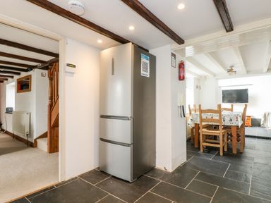 Kitchen area with a refrigerator next to a dining table and chairs at Forge Cottage in Sennen