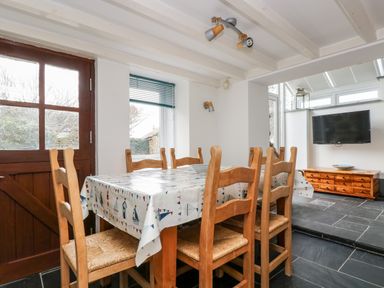 A dining area with wooden chairs and table with tablecloth near a wooden door and window at Forge Cottage in Sennen