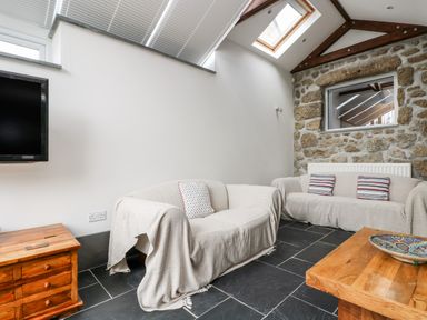 A sitting room with two sofas a wooden coffee table a small wooden cabinet and a stone wall at Forge Cottage in Sennen