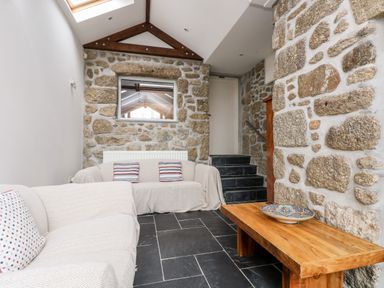 A seating area with two sofas a wooden table with a decorative bowl stone walls and black tiled floor at Forge Cottage in Sennen