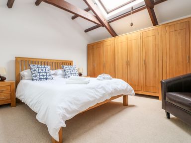 A bedroom with a wooden bed white bedding blue patterned pillows wooden wardrobes and a black armchair at Forge Cottage in Sennen