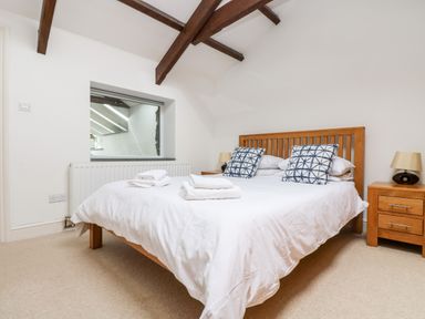 A bedroom with a wooden bed with white bedding and patterned pillows at Forge Cottage in Sennen