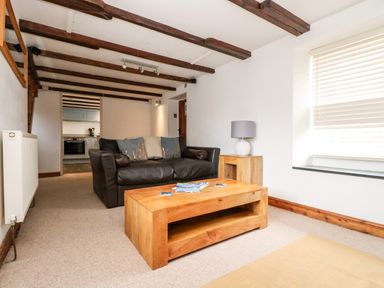 A living room with a brown leather sofa wooden coffee table side table with lamp and window with blinds at Forge Cottage in Sennen