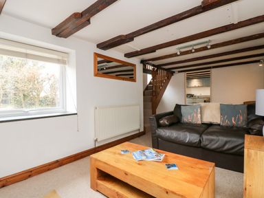 A living room with a black sofa a wooden coffee table a window and wooden ceiling beams at Forge Cottage in Sennen