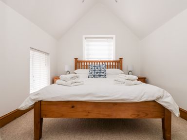 A bedroom with a wooden bed frame white bedding two bedside tables and lamps at Forge Cottage in Sennen