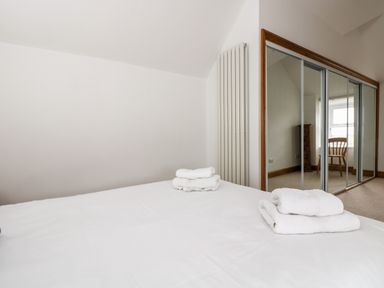 A bedroom with a bed and folded white towels on it a mirrored wardrobe and a wooden chair at Forge Cottage in Sennen