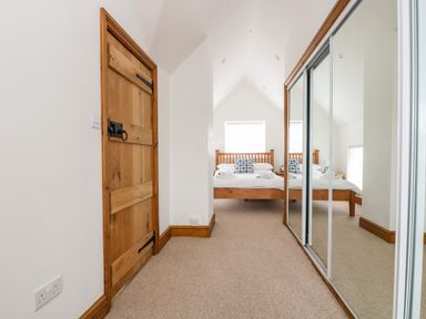 A bedroom with a wooden bed a window a mirrored wardrobe and a wooden door at Forge Cottage in Sennen