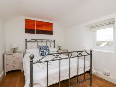 A bedroom with a metal bed frame white bedding bedside tables lamps and a triptych painting above the bed at Forge Cottage in Sennen