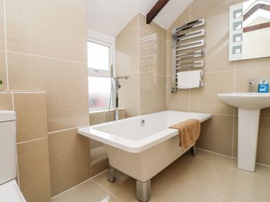 A bathroom with a bathtub, pedestal sink, toilet, towel radiator, and window at Forge Cottage in Sennen
