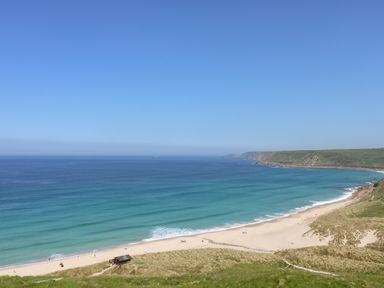 A beach with light sand and blue ocean water with cliffs in the background at Forge Cottage in Sennen