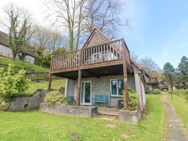 An outdoor view of a two-story wooden lodge with balcony and patio at Valley Lodge 44 in Callington