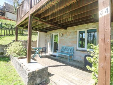 A covered wooden patio with a blue bench a table and chair outside a stone house at Valley Lodge 44 in Callington