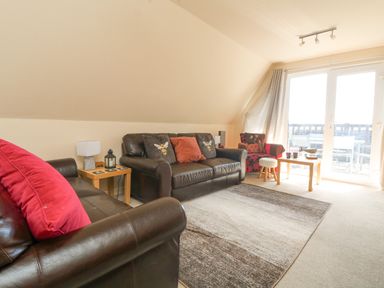 A living room with two brown leather sofas a red patterned armchair a wooden coffee table and large windows at Valley Lodge 44 in Callington