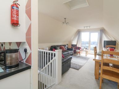 A living room with black sofas a dining table and chairs a coffee maker on a kitchen counter and a fire extinguisher on the wall at Valley Lodge 44 in Callington