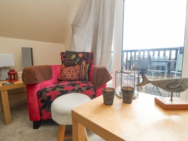 A chair with cushions next to a small table with decorative items by a sliding glass door at Valley Lodge 44 in Callington