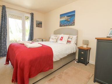 A bedroom with a bed laid with a red blanket and pillows next to a window with blue curtains at Valley Lodge 44 in Callington