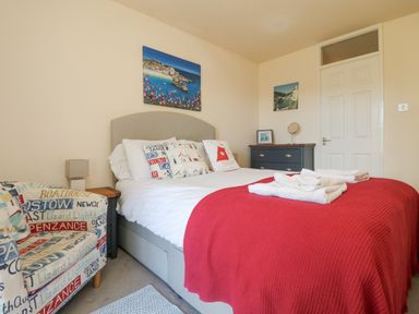 A bedroom with a double bed covered with white and red bedding beside a chair with printed text at Valley Lodge 44 in Callington